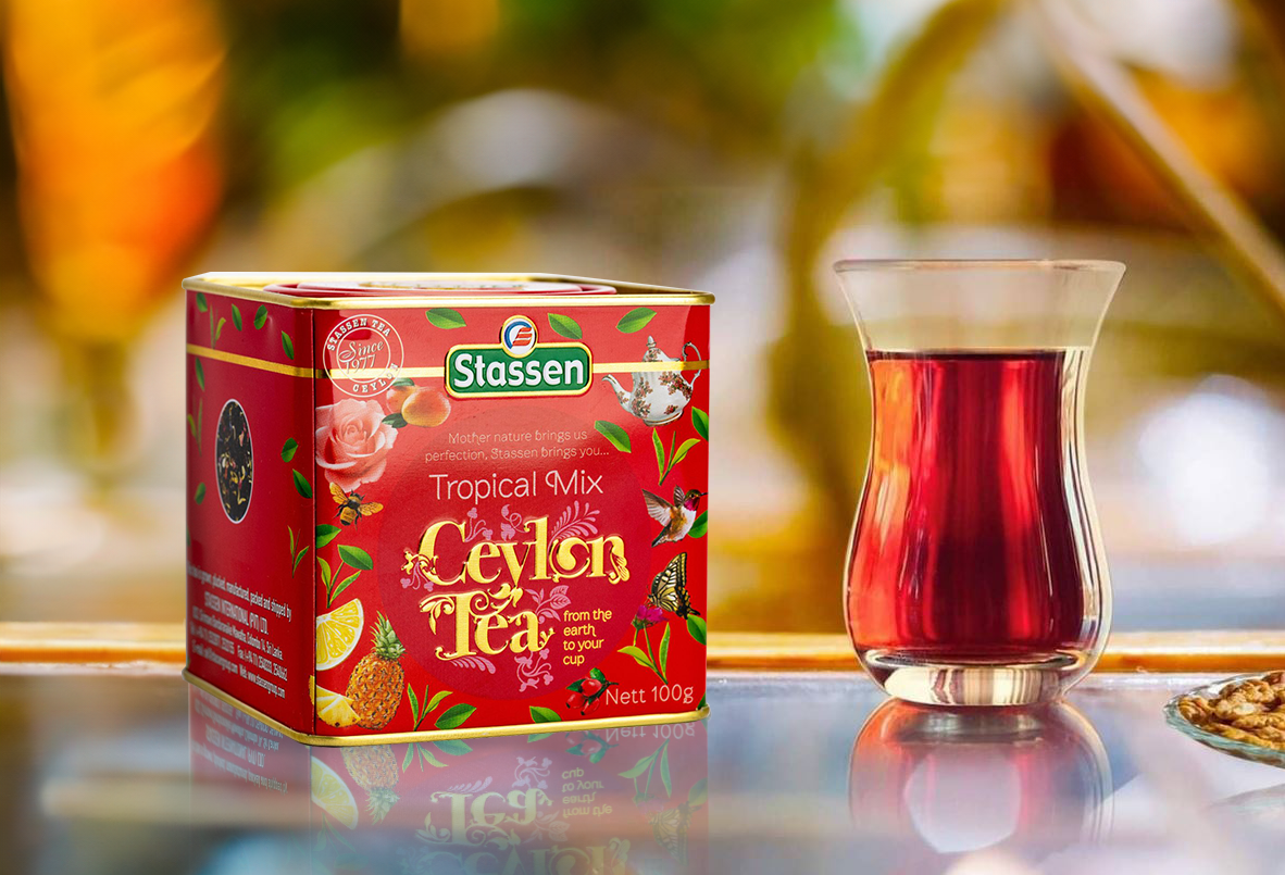 Herbata Tropical Mix Stassen w puszce obok szklanki z ciemnoczerwonym naparem.