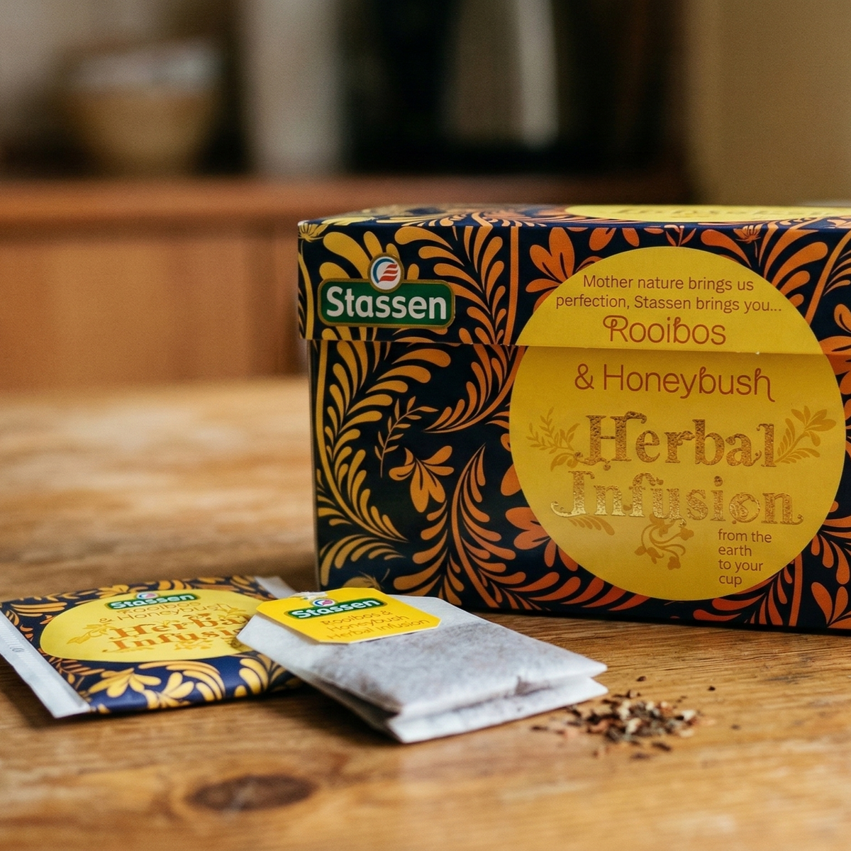 Opakowanie herbaty ziołowej Stassen Rooibos & Honeybush oraz saszetki herbaty na drewnianym stole.