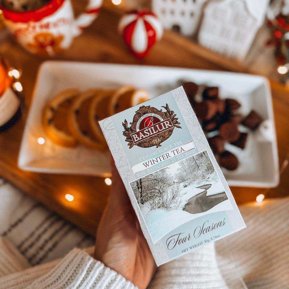 Herbata Basilur Winter Tea w zimowej aranżacji z suszonymi pomarańczami, czekoladą i świątecznymi lampkami