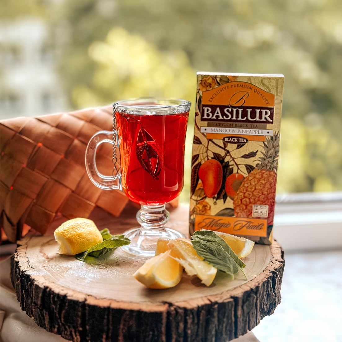 Herbata Basilur Mango & Pineapple z filiżanką naparu, cytryną i miętą na drewnianej podstawce