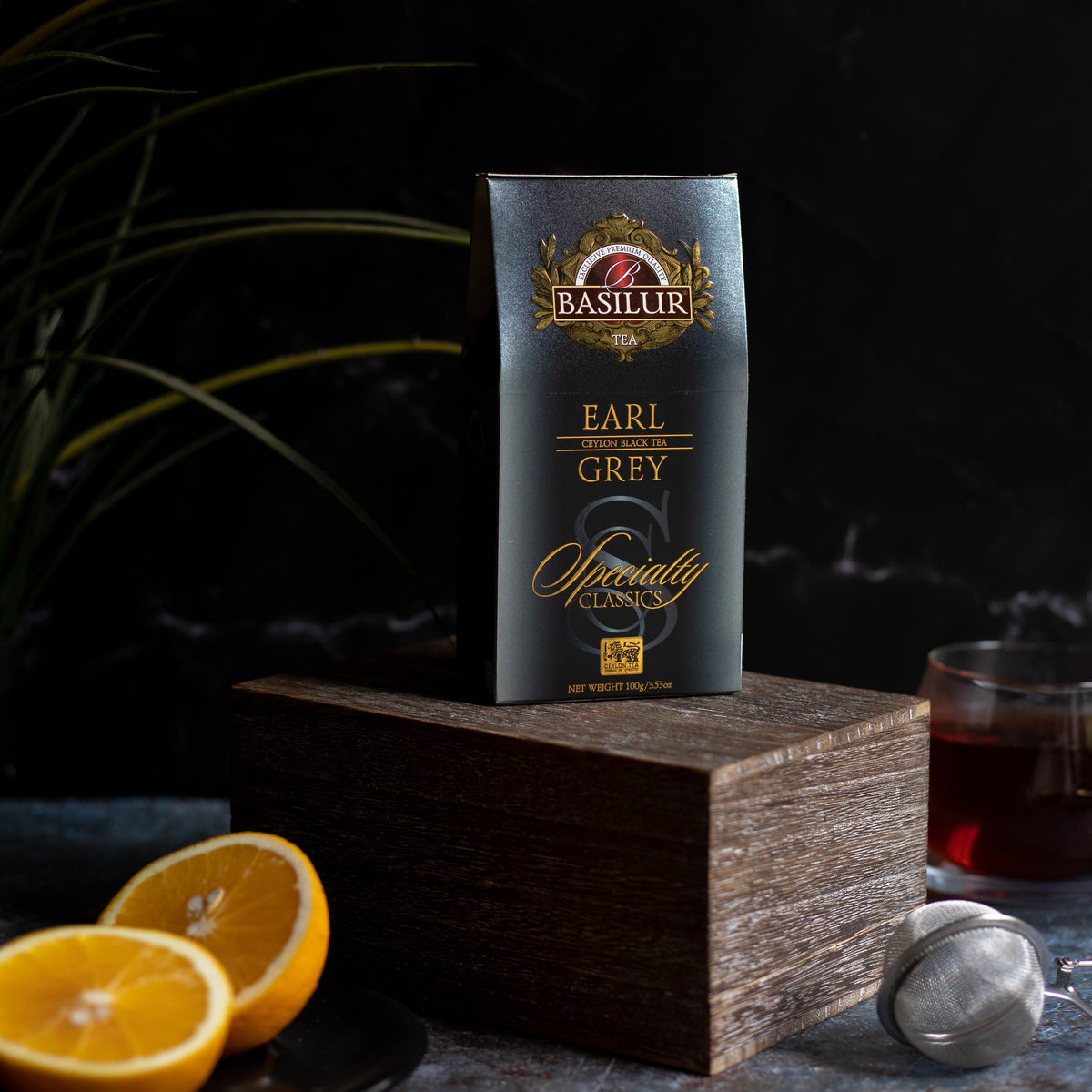 Opakowanie herbaty Basilur Earl Grey ustawione na drewnianym podwyższeniu obok plasterków cytryny i szklanki z naparem.