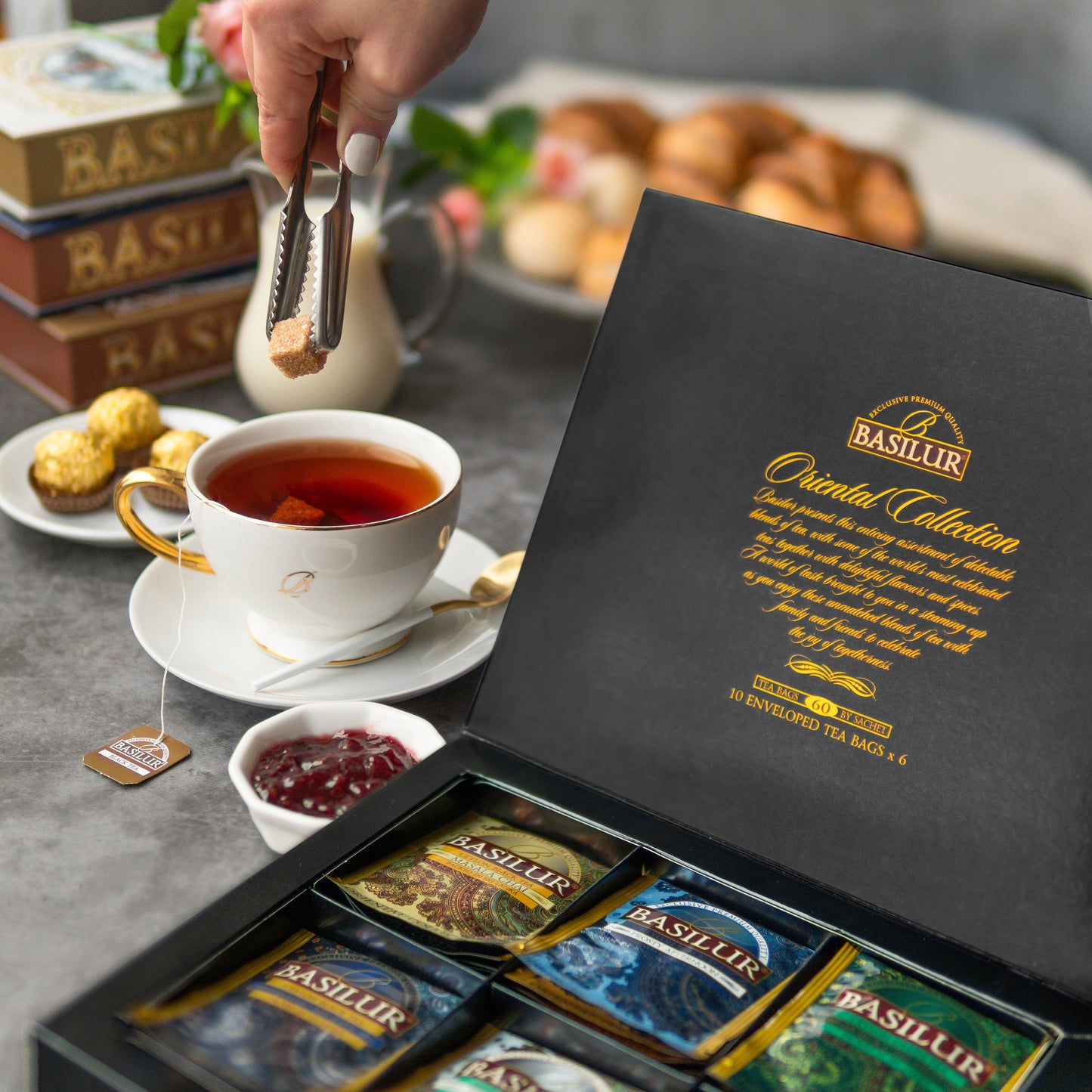 Zestaw herbat Basilur Oriental Assorted w eleganckim pudełku obok filiżanki gorącej herbaty i dodatków.