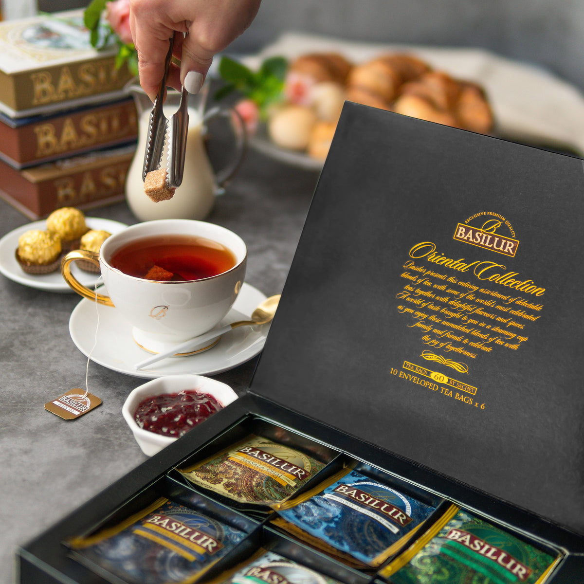 Zestaw herbat Basilur Oriental Assorted w eleganckim pudełku obok filiżanki gorącej herbaty i dodatków.