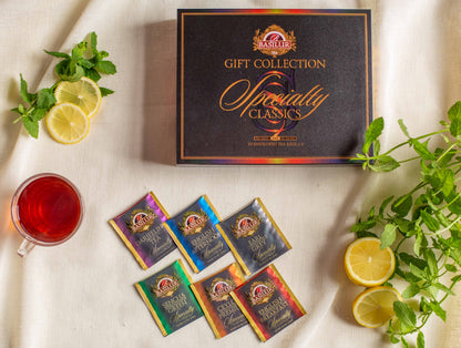 Zamknięte pudełko Basilur Gift Collection Specialty Classics ustawione na jasnym tle w otoczeniu saszetek herbat cytryny mięty oraz filiżanki czerwonej herbaty. Kompozycja eksponuje luksusowy styl zestawu oraz różnorodność klasycznych herbat Basilur.
