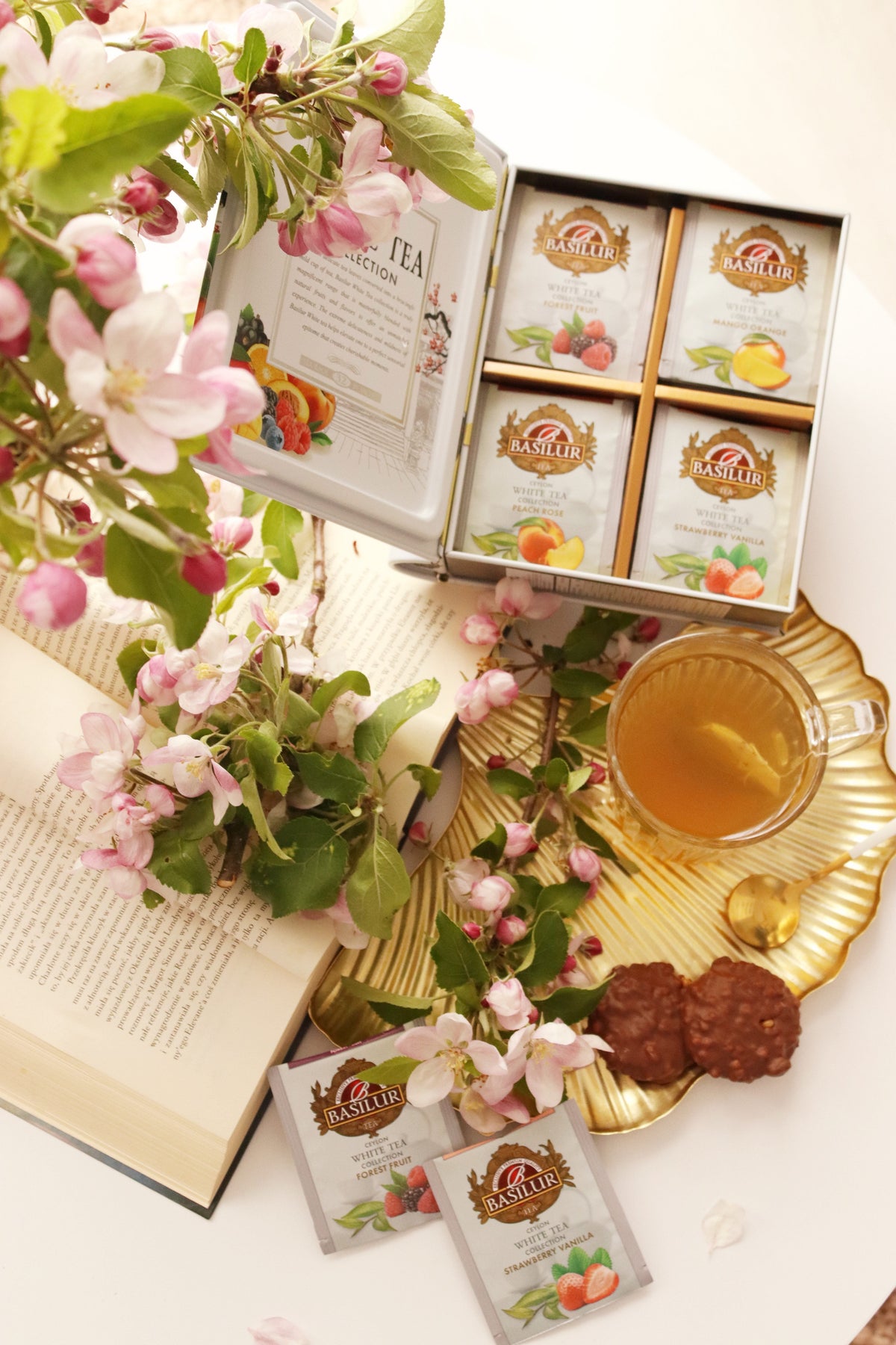 Zestaw białych herbat Basilur White Tea Assorted w kopertach, filiżanka naparu i różowe kwiaty