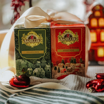 Herbaty Basilur Orange Spice i Spiced Wine przewiązane białą kokardą, wśród czerwonych bombek i świątecznych dekoracji.