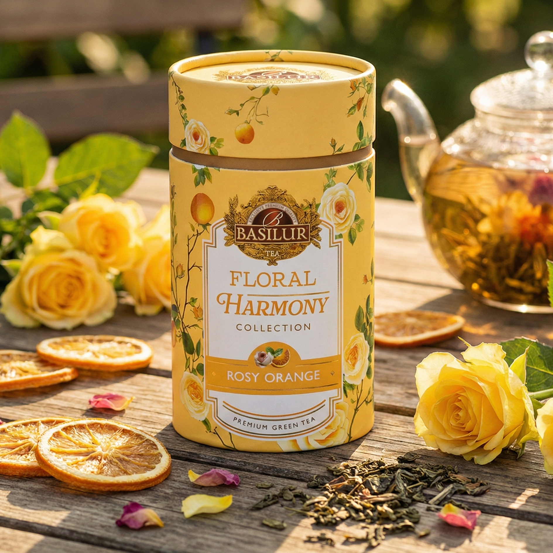 Opakowanie herbaty Basilur Floral Harmony Rosy Orange na drewnianym stole, obok żółtych róż, suszonych plasterków pomarańczy i dzbanka z herbatą.