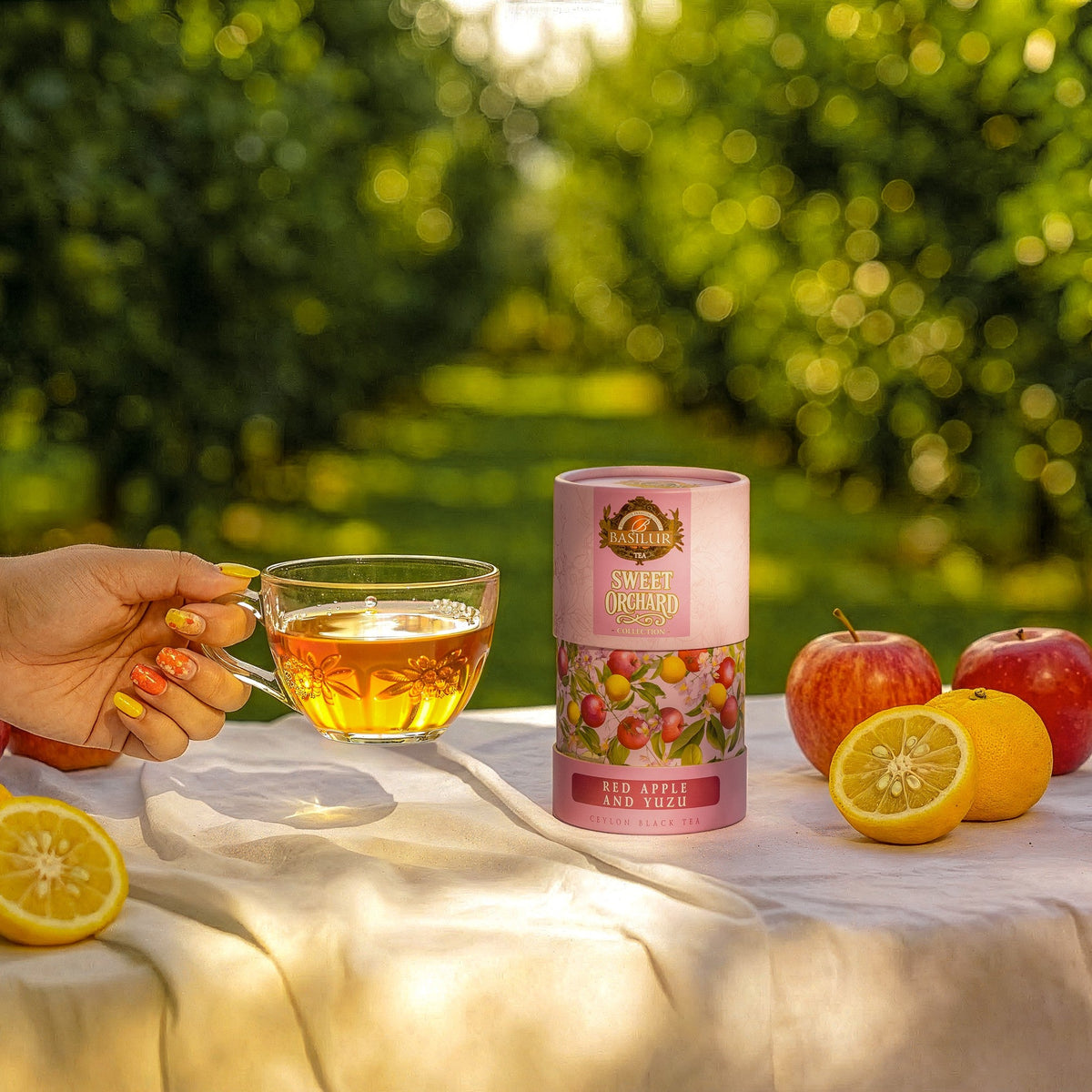 Herbata Basilur Red Apple and Yuzu obok szklanej filiżanki z naparem, czerwonych jabłek i przekrojonych cytrusów