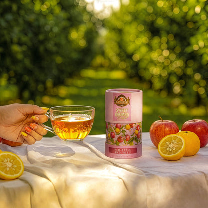 Herbata Basilur Red Apple and Yuzu obok szklanej filiżanki z naparem, czerwonych jabłek i przekrojonych cytrusów